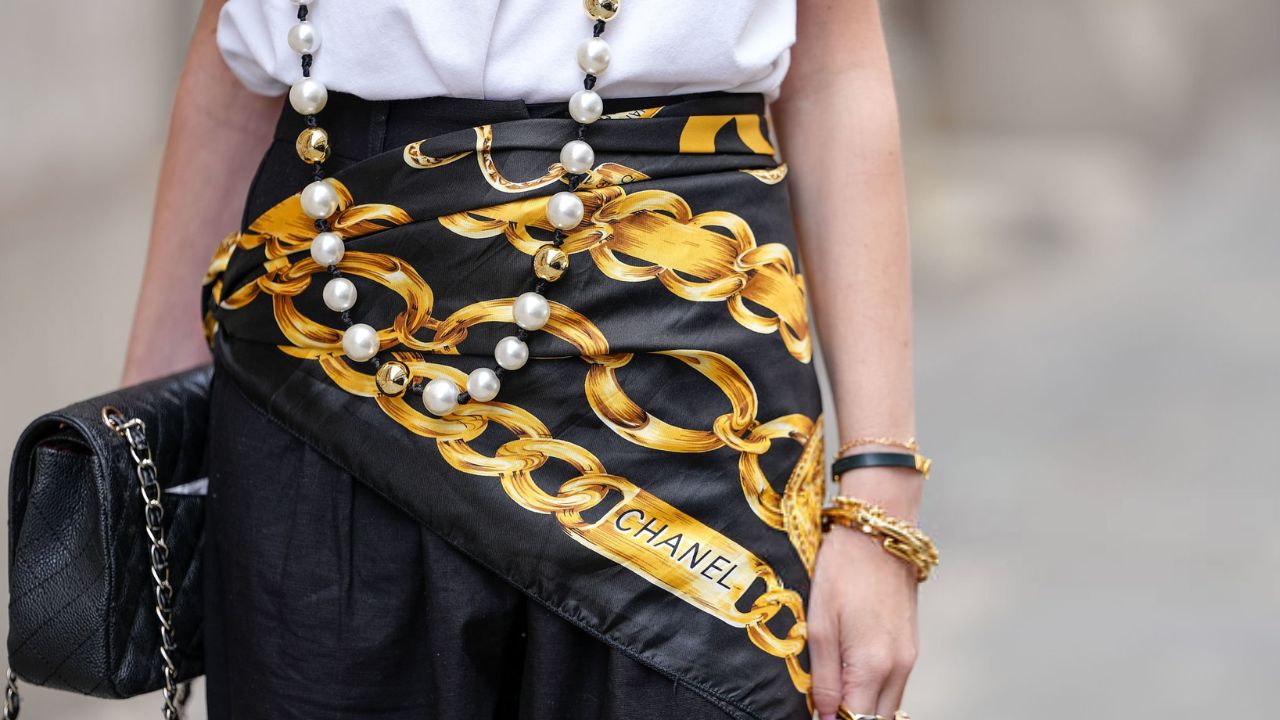 Lenço de seda Chanel estampado em preto e dourado combinado com um longo colar de pérolas e ouro | Reprodução/Edward Berthelot/Getty Images Embed