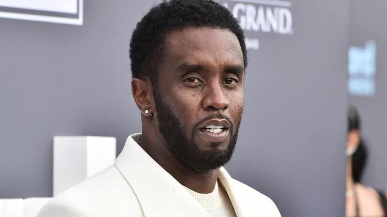 Na imagem, vemos o rapper Sean "Diddy" Combs sendo levado para a penitênciaria sob os olhares e lentes de uma multidão ao fundo.