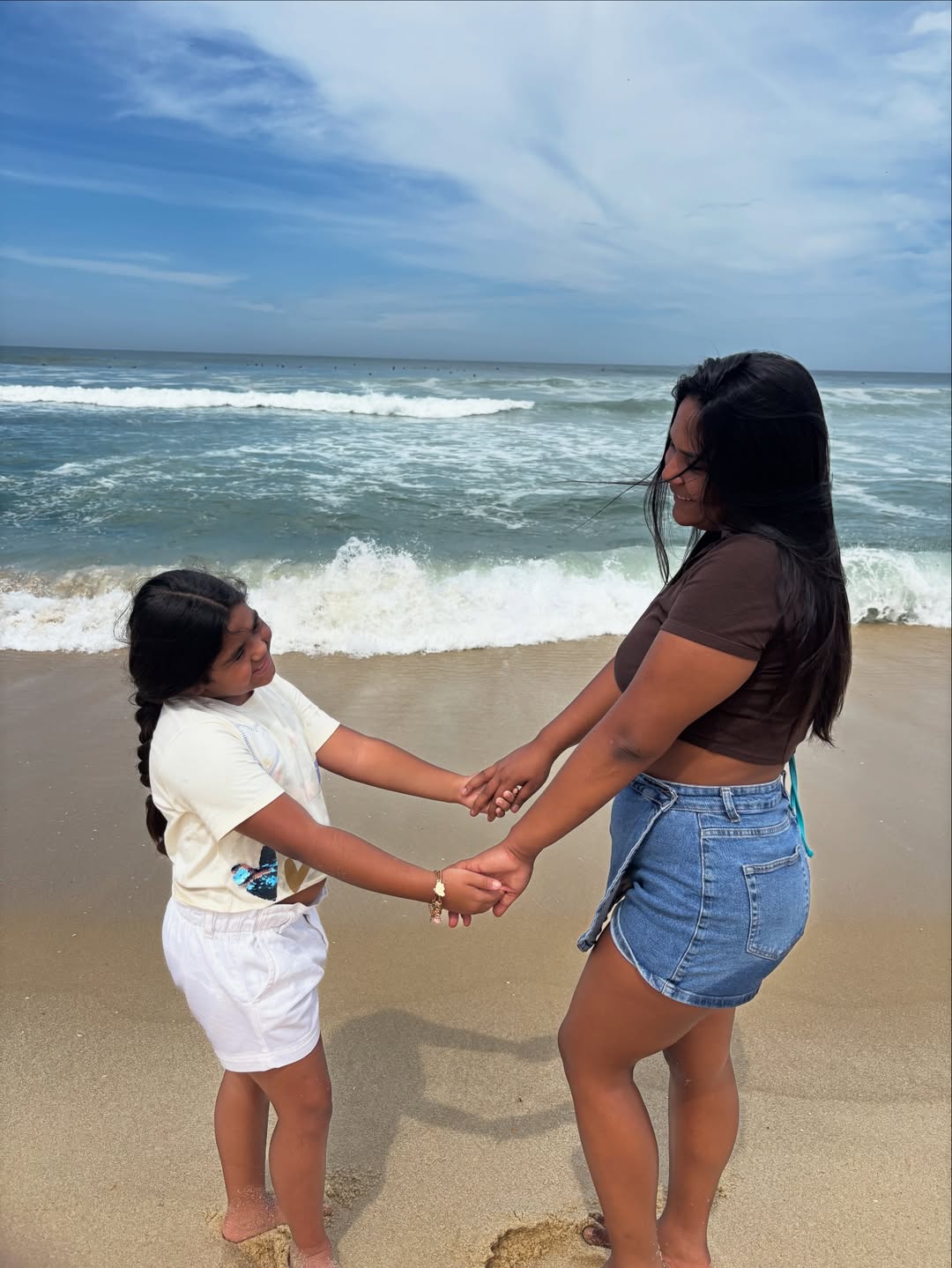 Chaiany e Lara, mulher morena e filha, de mãos dadas em praia