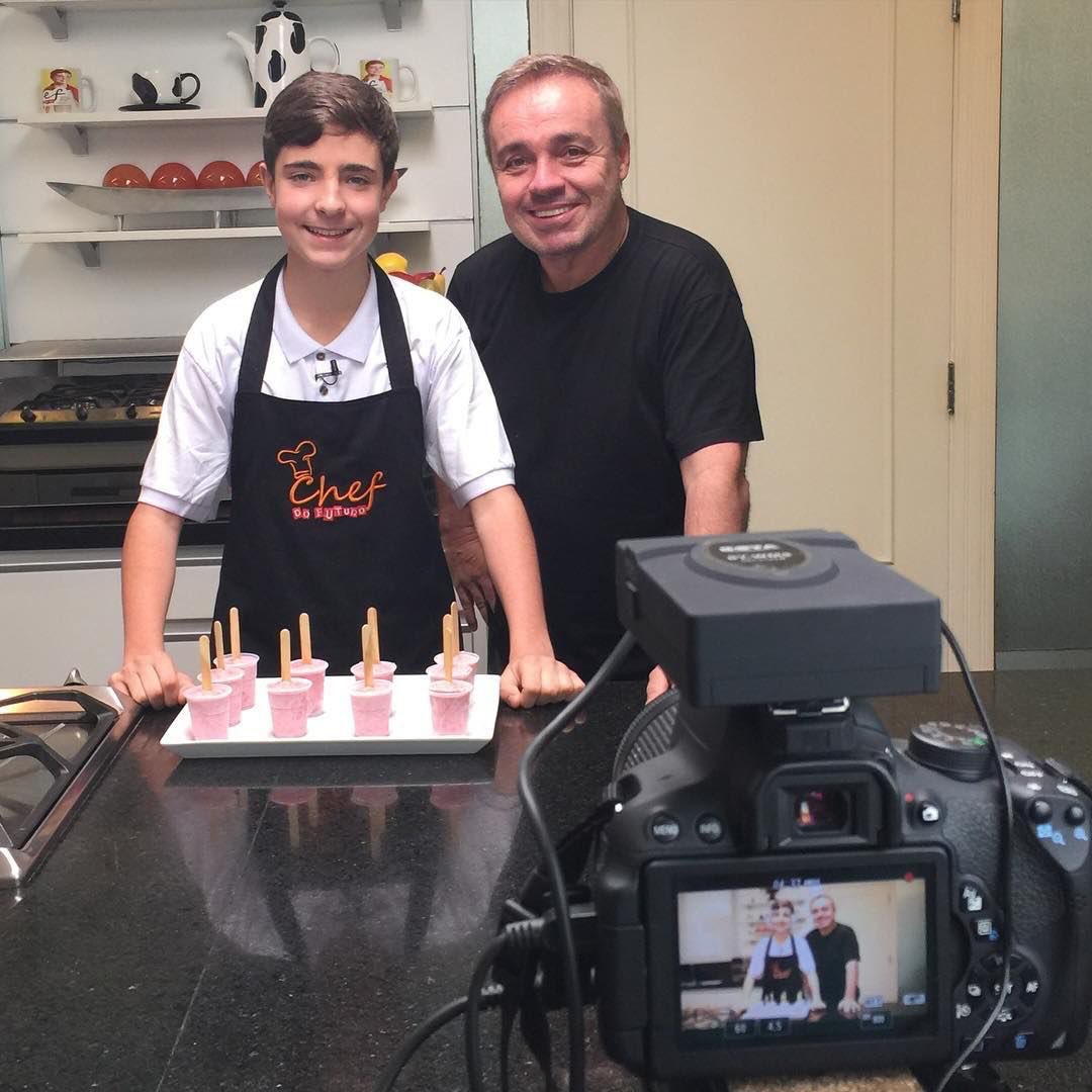 João Augusto ainda criança aparece ao lado de Gugu Liberato em cozinha, durante gravação, com bolo e velas sobre a mesa