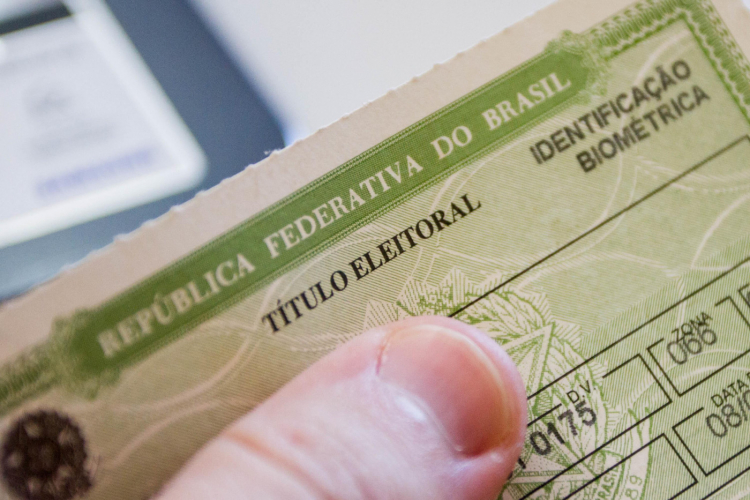 Close de um título de eleitor brasileiro sendo segurado por uma pessoa, com destaque para a área de identificação biométrica no documento